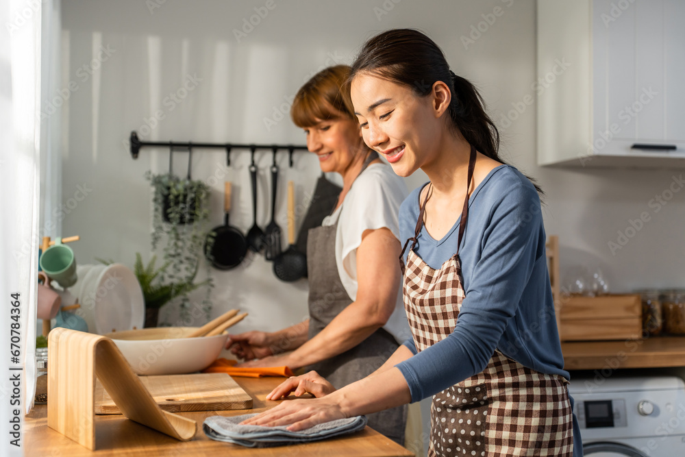 Caucasian senior elderly woman cleaning kitchen in house with daughter. 