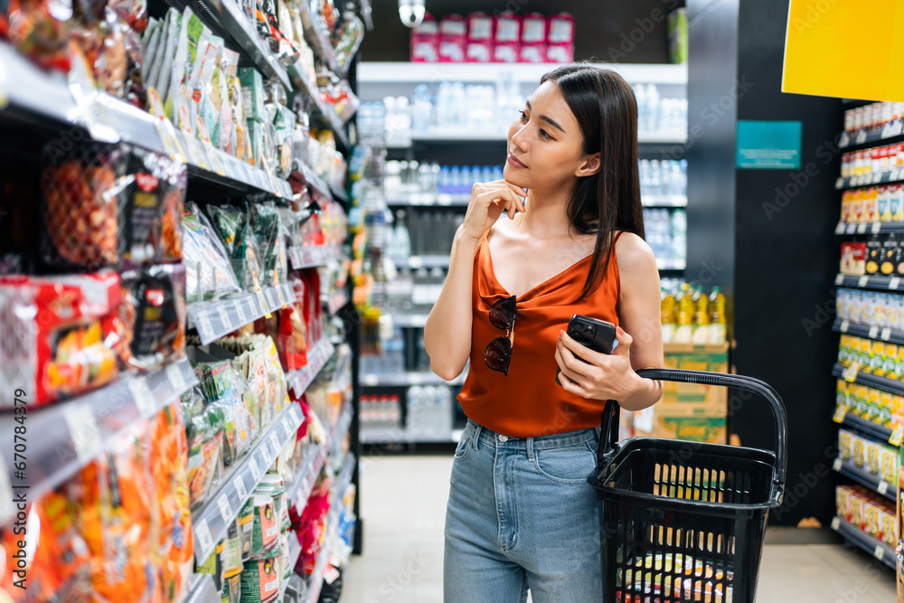 Asian young beautiful woman holding grocery basket walk in supermarket. 