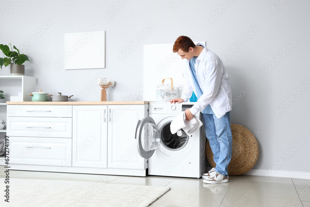 Young man putting laundry into washing machine at home