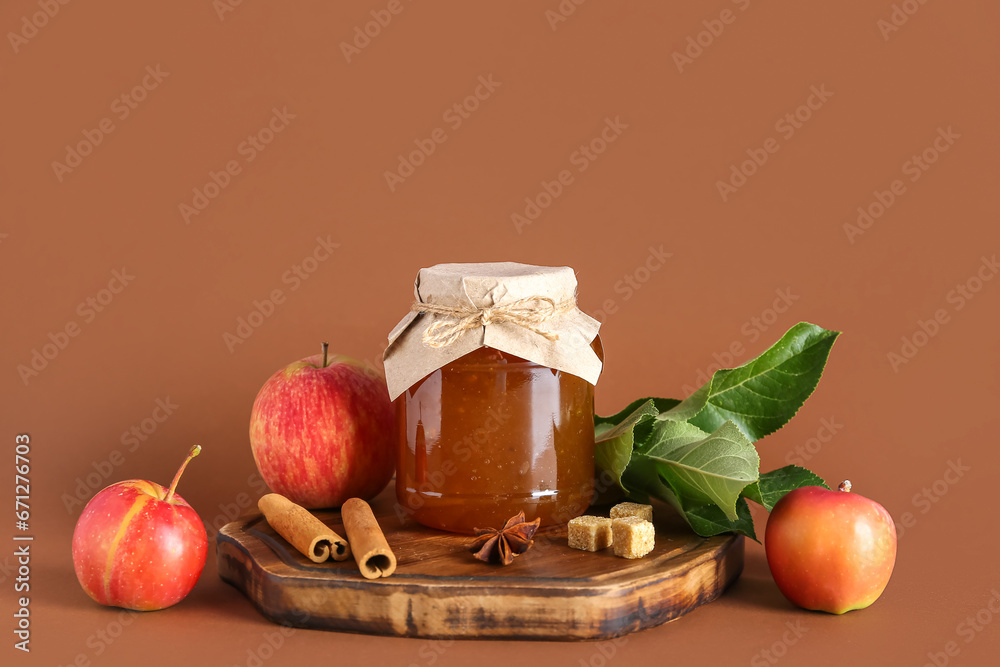 Wooden board with jar of tasty apple jam and ingredients on color background