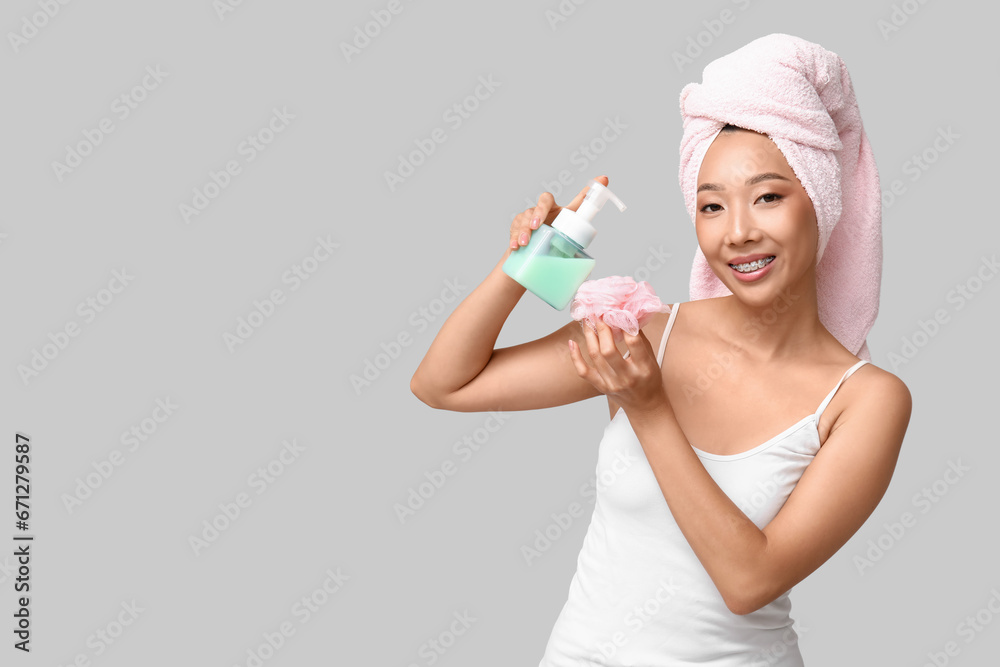 Young Asian woman with shower gel and loofah on light background