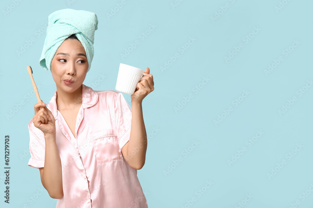 Young Asian woman with toothbrush and cup on blue background