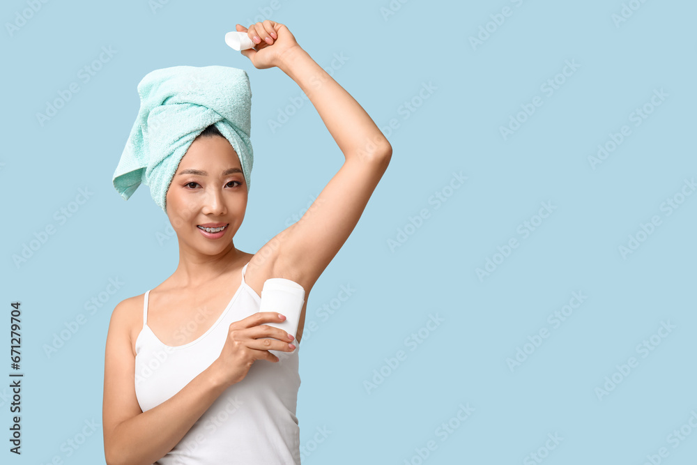 Young Asian woman using deodorant on blue background