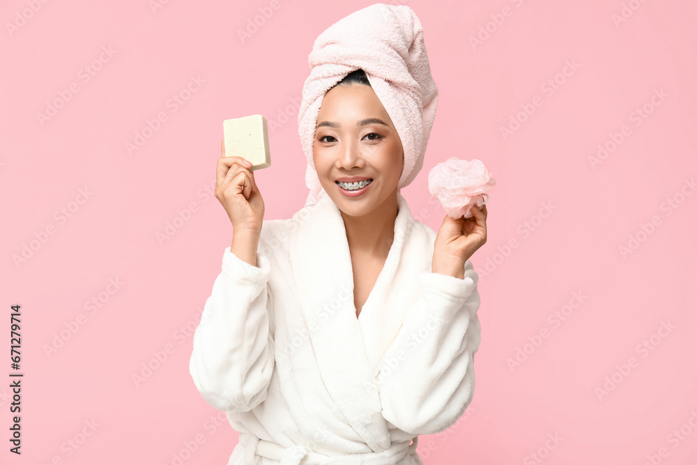 Young Asian woman with soap and loofah on pink background