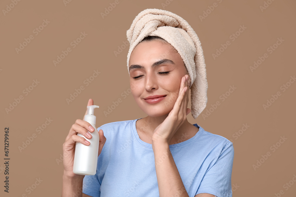 Young woman with bottle of cream on brown background, closeup