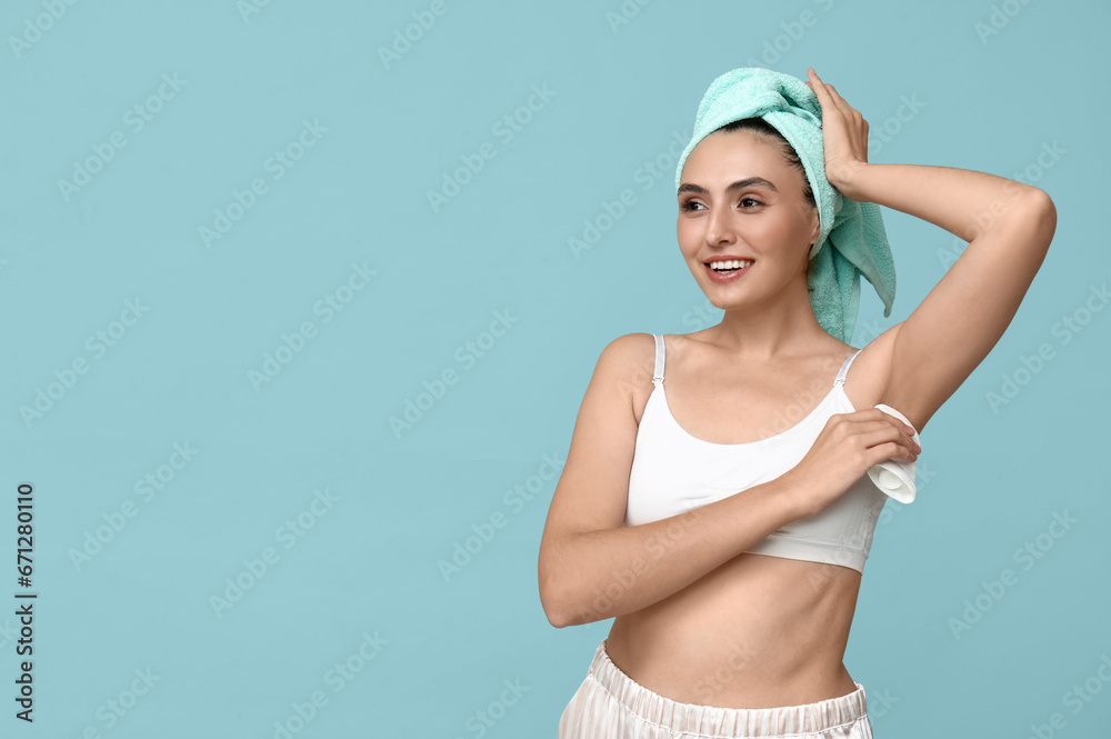 Young woman using deodorant on blue background