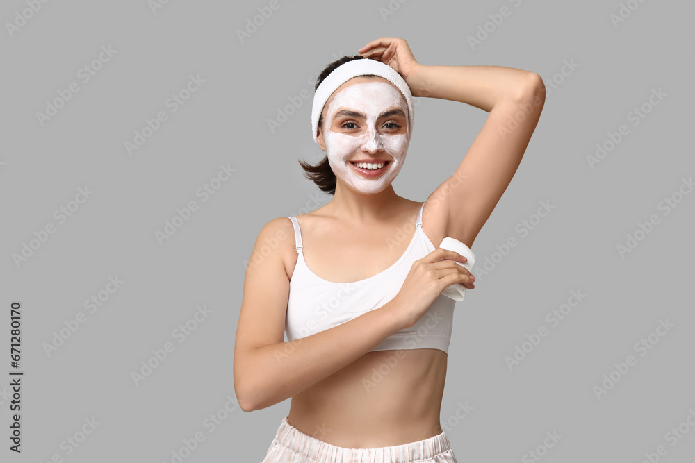 Young woman using deodorant on light background