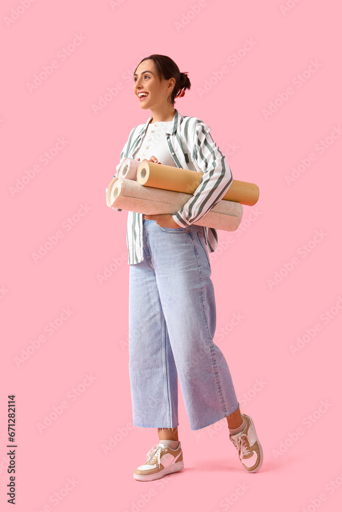 Young woman with wallpaper rolls on pink background