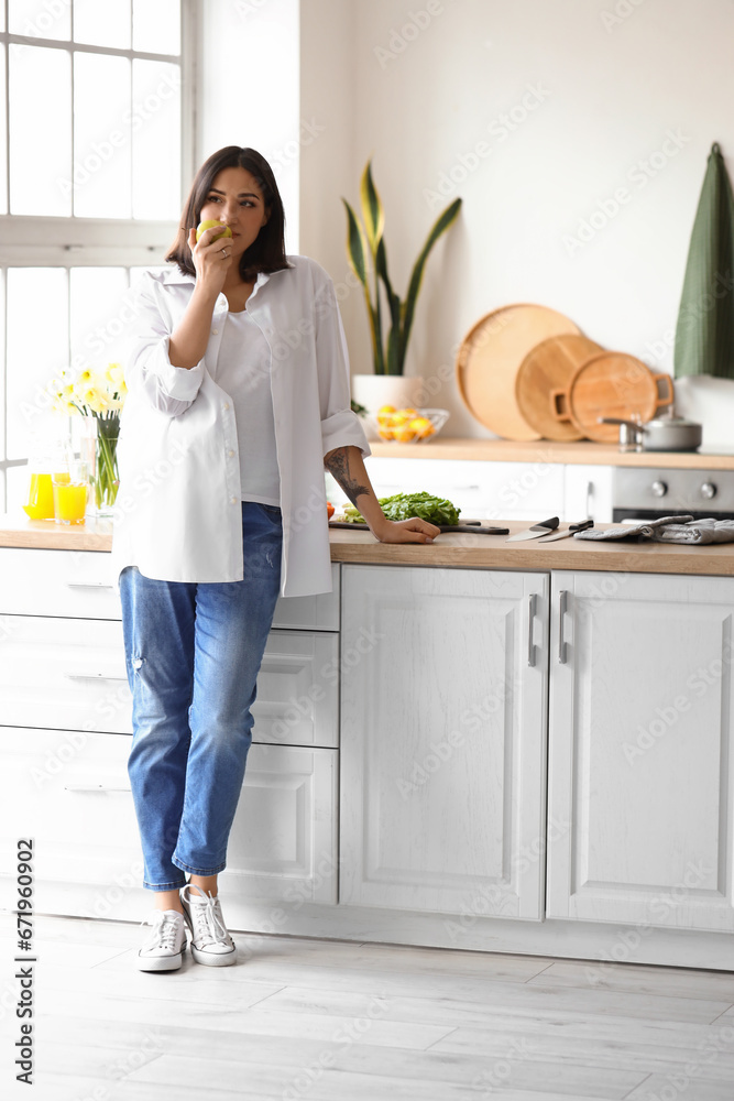 Young pregnant woman with apple in kitchen