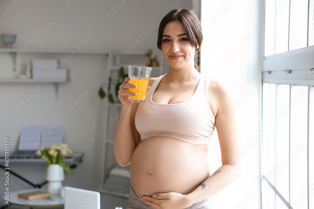 Sporty young pregnant woman with glass of juice at home