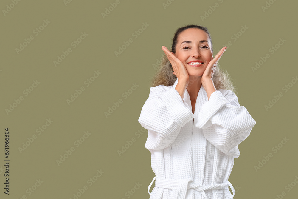 Beautiful mature woman giving herself face massage on khaki background