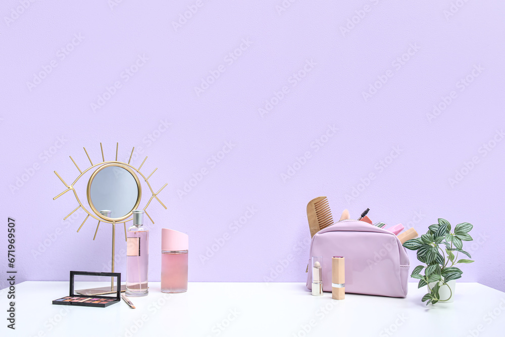 Different makeup products and mirror on dressing table near purple wall in room