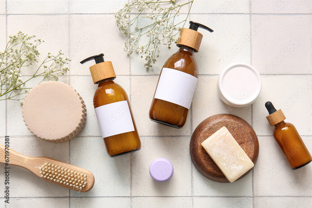 Bottles of shampoo, brush, soap bar and cosmetic products on white tile background