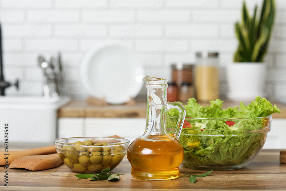 Jug with oil, olives and fresh salad on table in kitchen