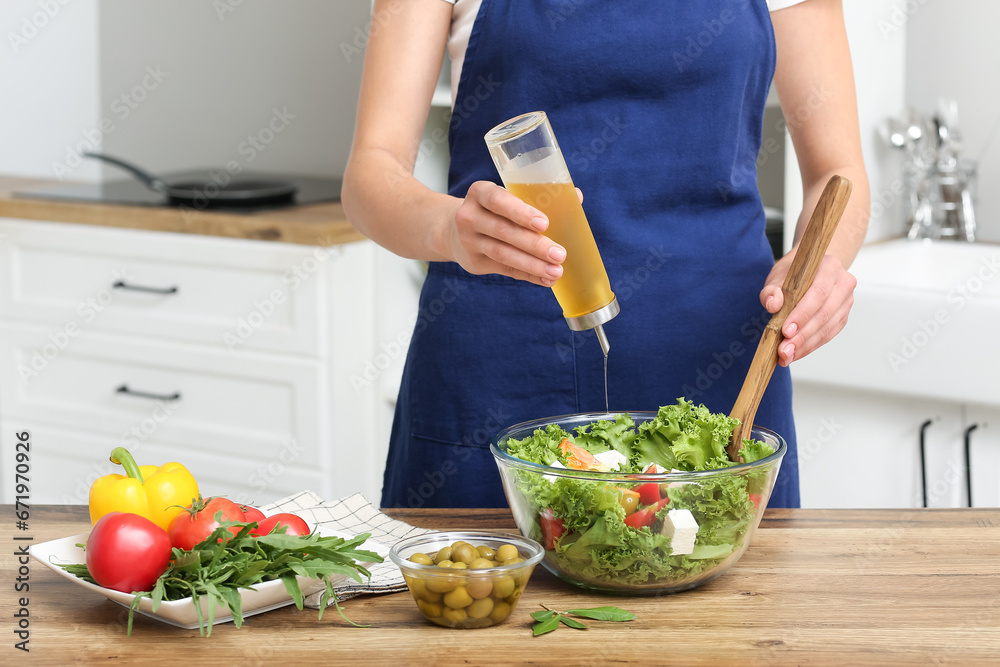 Woman adding olive oil into bowl with tasty salad at table in kitchen