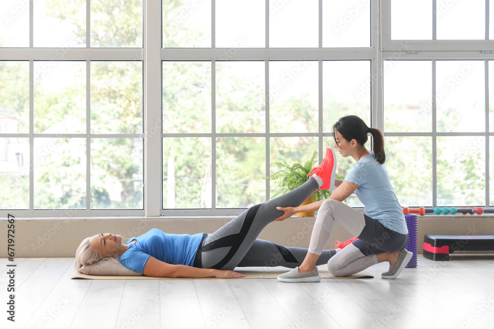 Mature woman training with therapist on mat in rehabilitation center