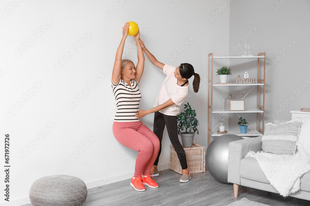 Mature woman training with ball and rehabilitation therapist at home