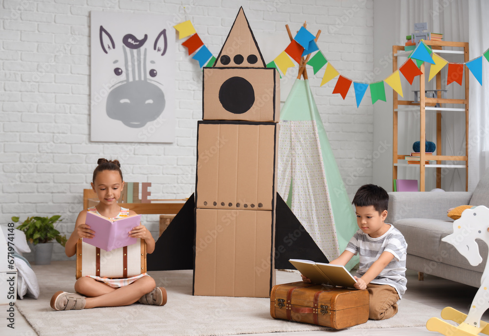 Cute little children with adventure books and cardboard rocket at home