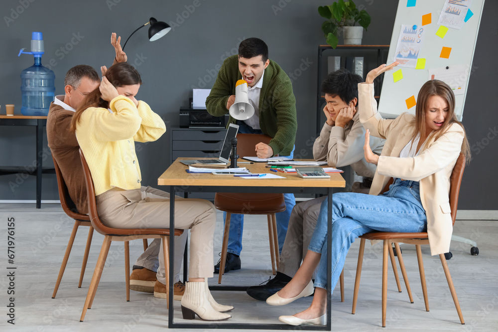 Angry young businessman with megaphone shouting at colleagues in office