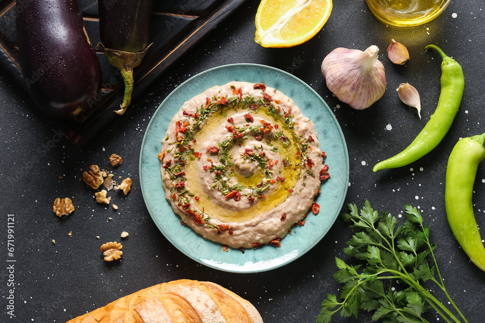 Plate of tasty baba ghanoush with ingredients on black background