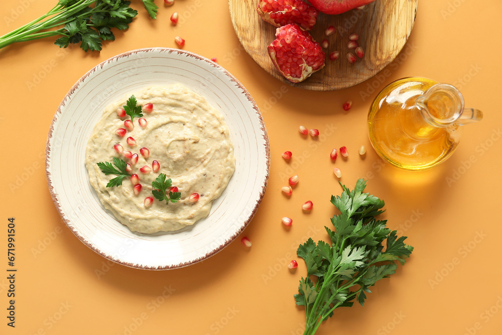 Plate of tasty baba ghanoush with oil and pomegranate on orange background