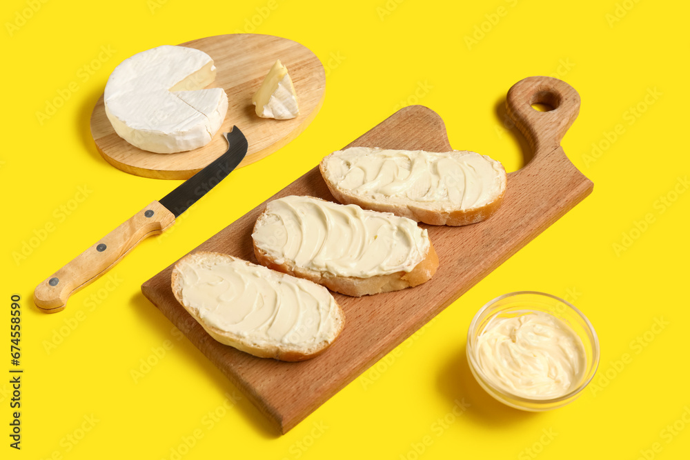 Wooden board of bread with butter and camembert on yellow background