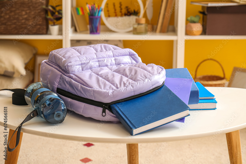 School backpack with books and bottle of water on table in room