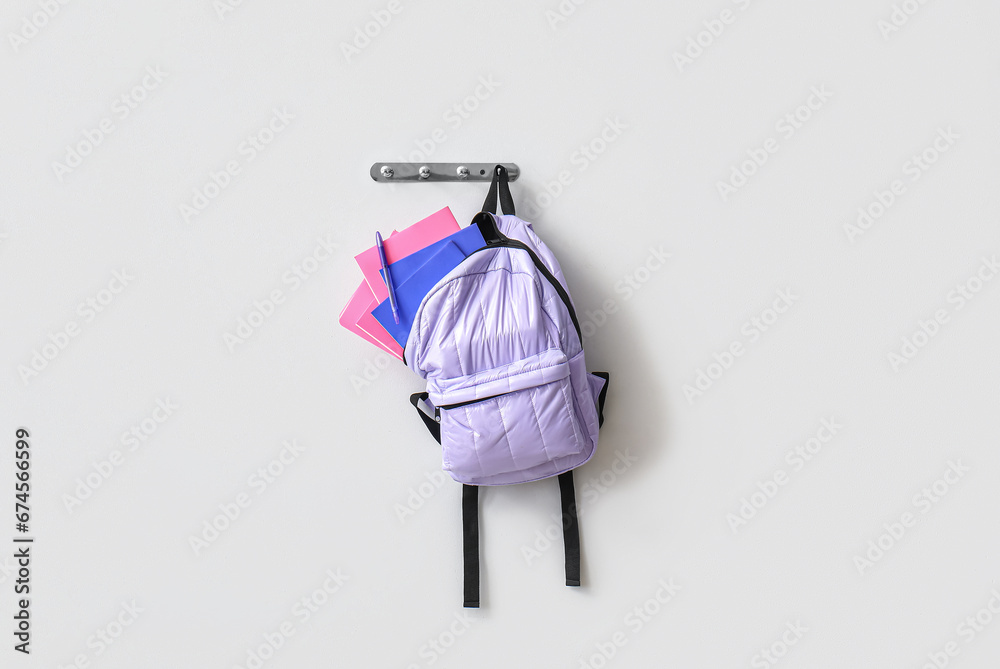 School backpack with stationery hanging on light wall