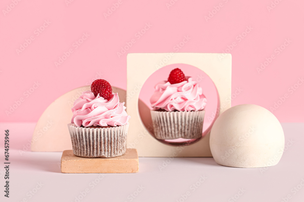 Decorative stand with tasty raspberry cupcakes on pink background