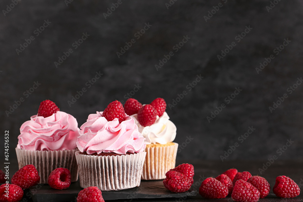 Board od tasty raspberry cupcakes and fresh berries on black background