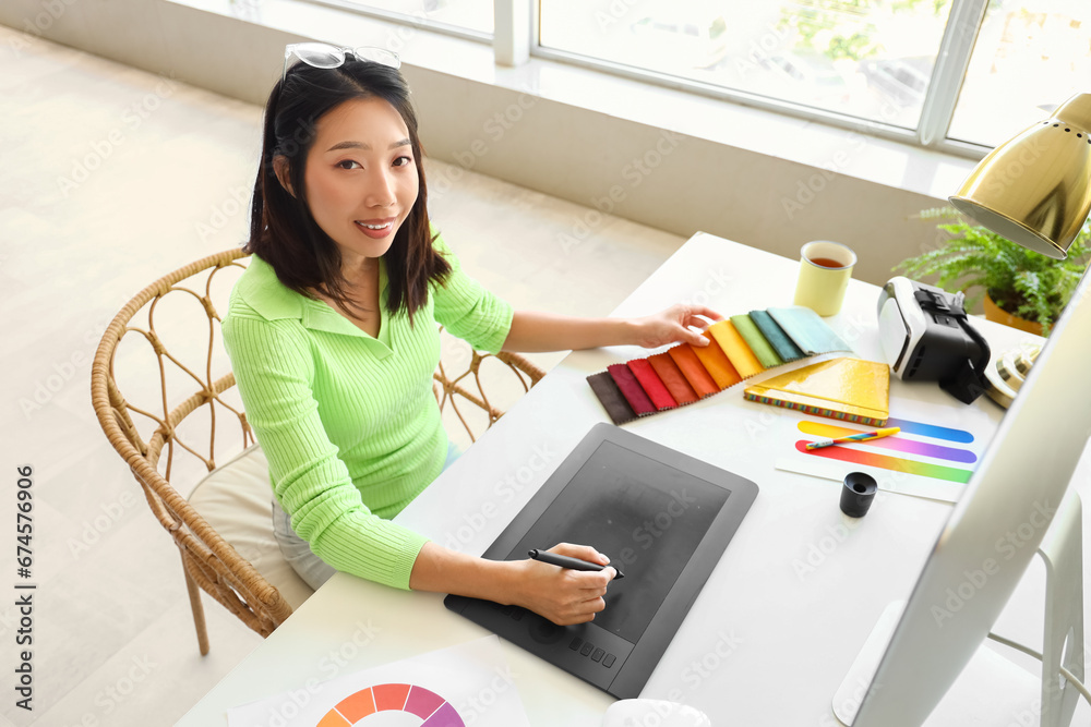 Asian interior designer working with graphic tablet and fabric samples in office