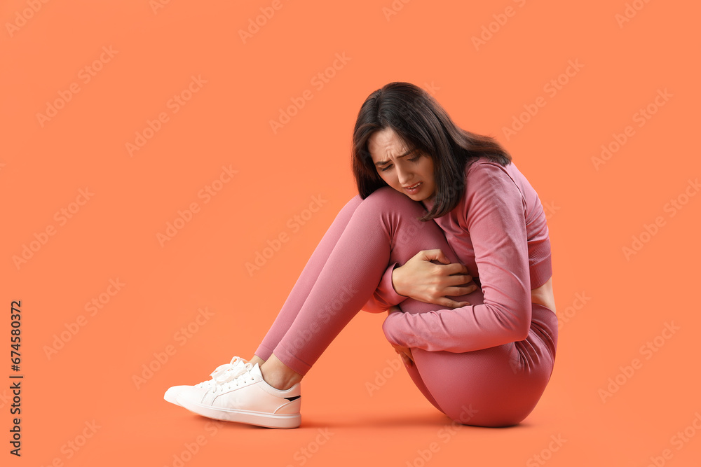 Beautiful young afraid woman sitting on orange background