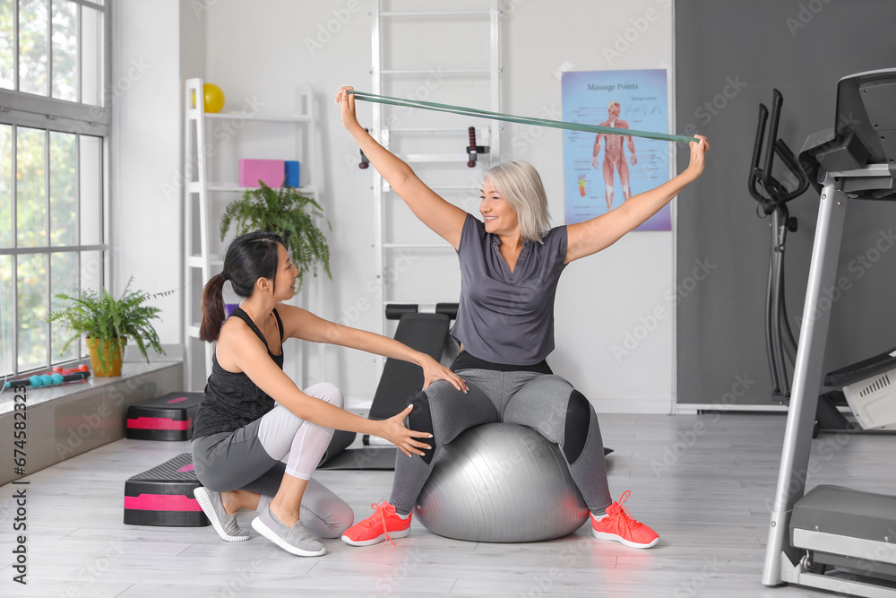 Mature woman training with therapist on fitball in rehabilitation center