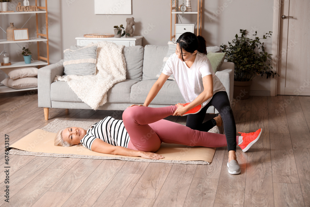 Mature woman training on mat with rehabilitation therapist at home