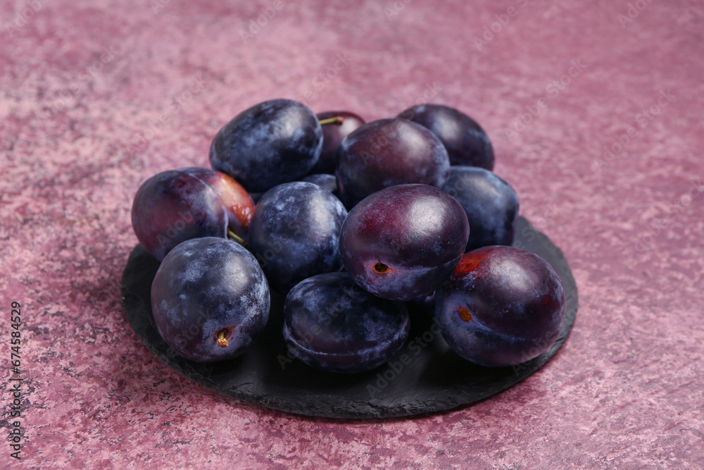 Black board with fresh plums on purple background