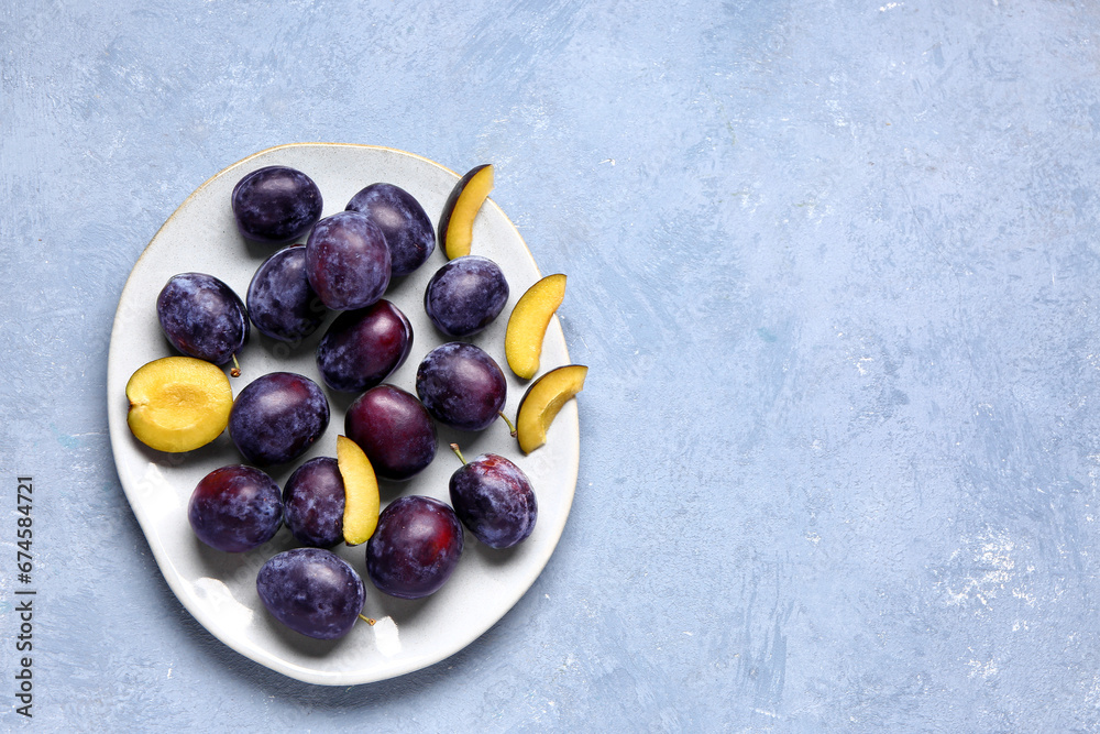 Plate with fresh plums on blue background