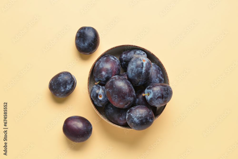 Bowl with fresh plums on yellow background