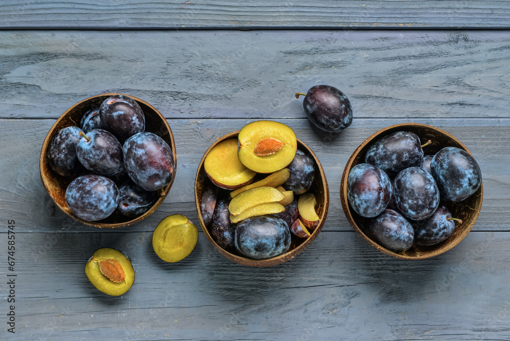 Bowls with fresh plums on blue wooden background