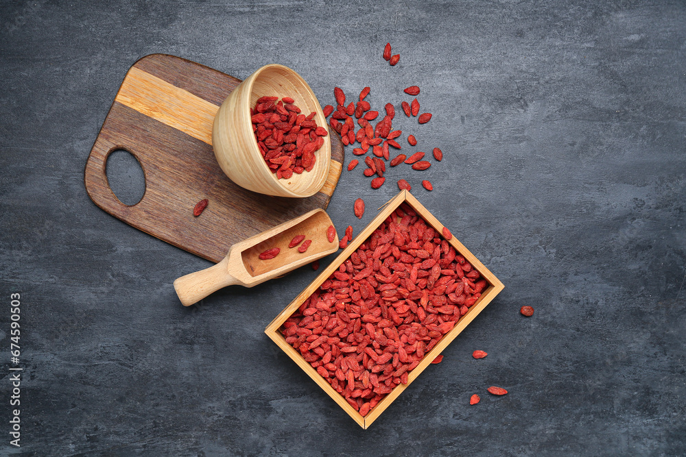 Wooden box and bowl with red dried goji berries on black background