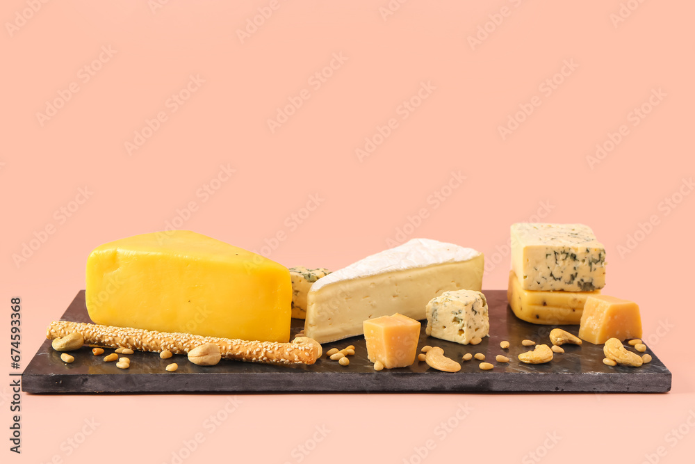 Board with tasty cheese, nuts and grissini on pink background