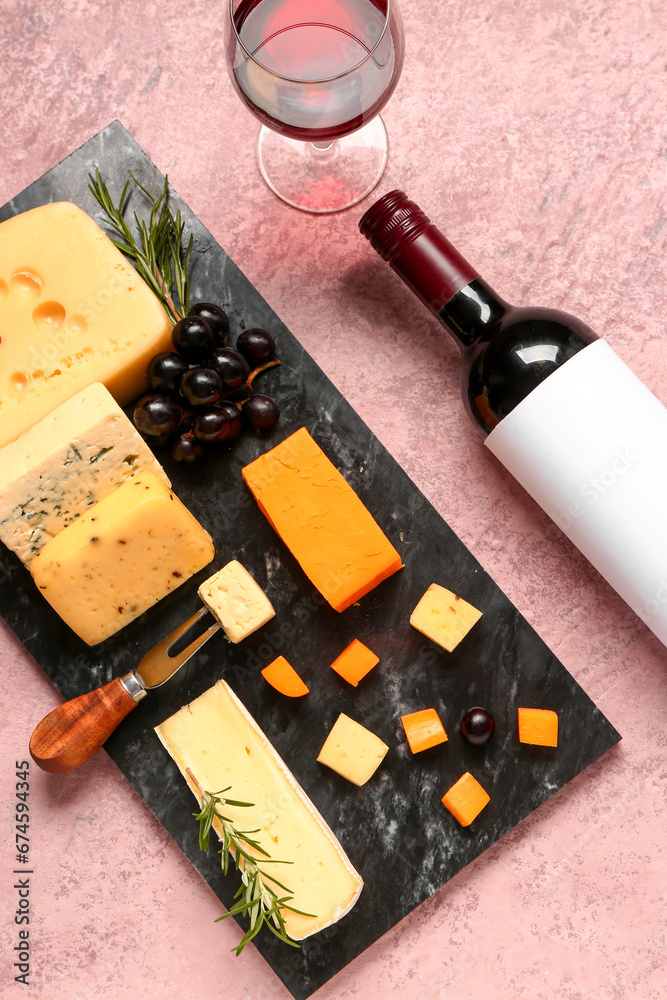 Board with tasty cheese, grapes, bottle and glass of wine on pink background