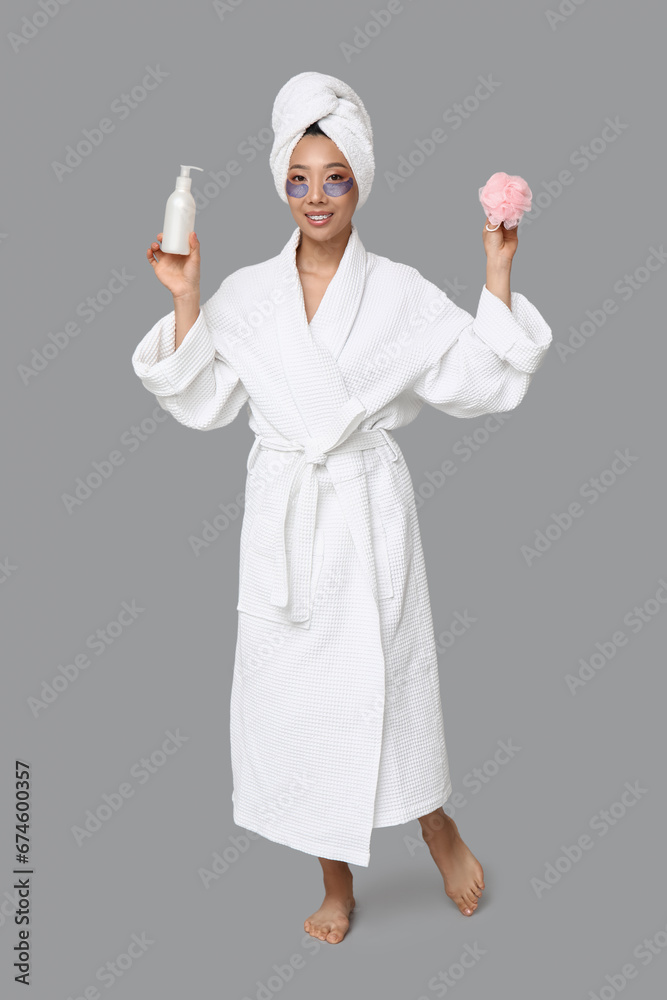 Young Asian woman with loofah and cosmetic bottle on light background