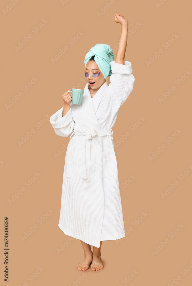 Young Asian woman with under-eye patches and coffee cup on brown background