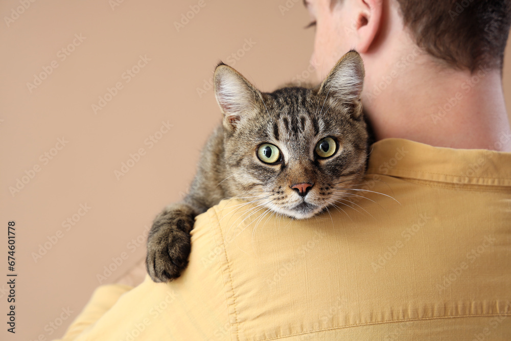 Young man with cute cat on beige background, closeup