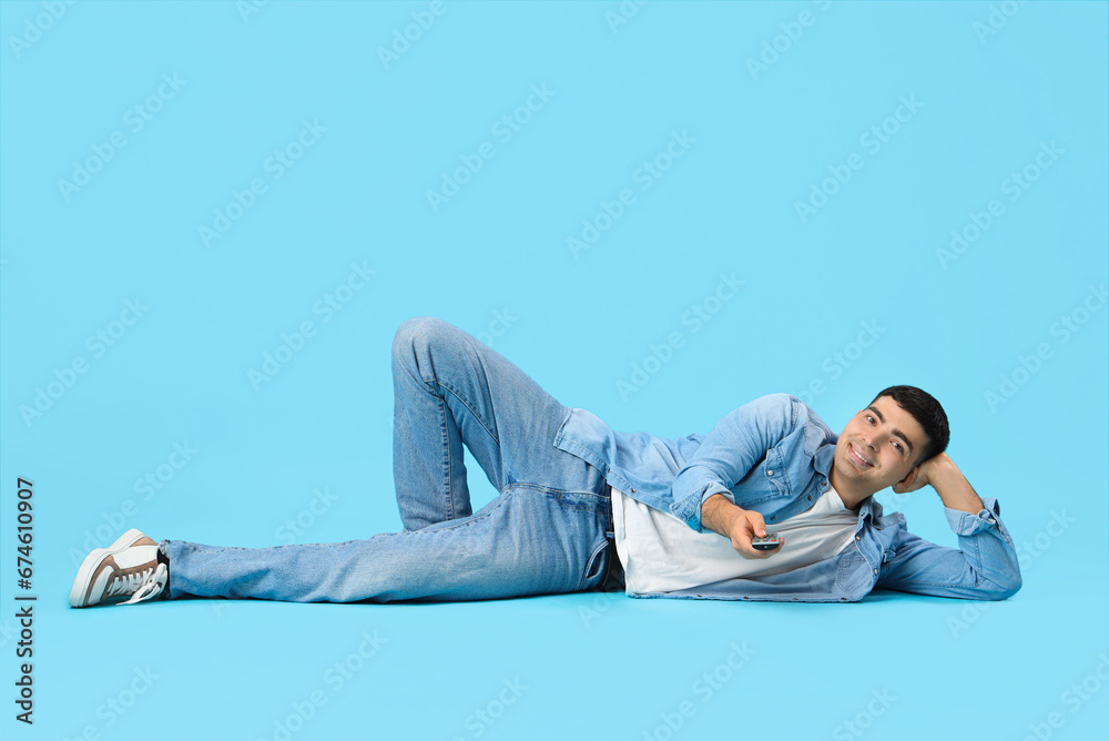 Handsome young man watching TV while lying on floor against blue background