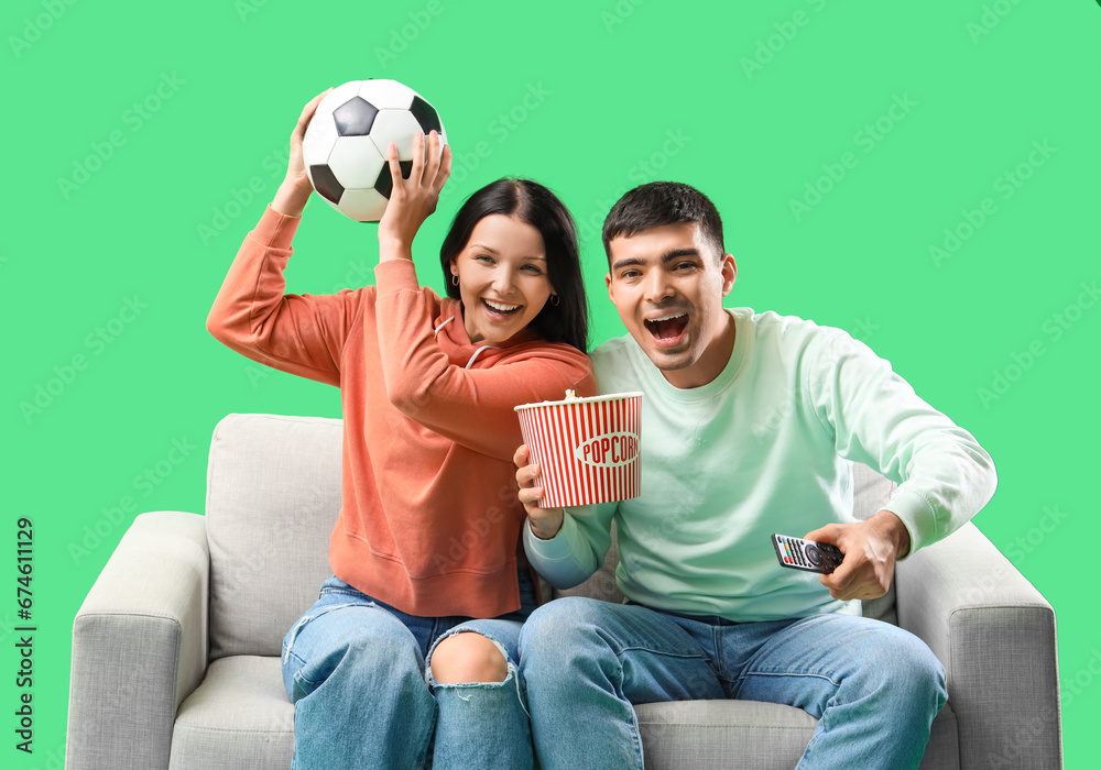 Cheerful young couple watching soccer match on TV against green background