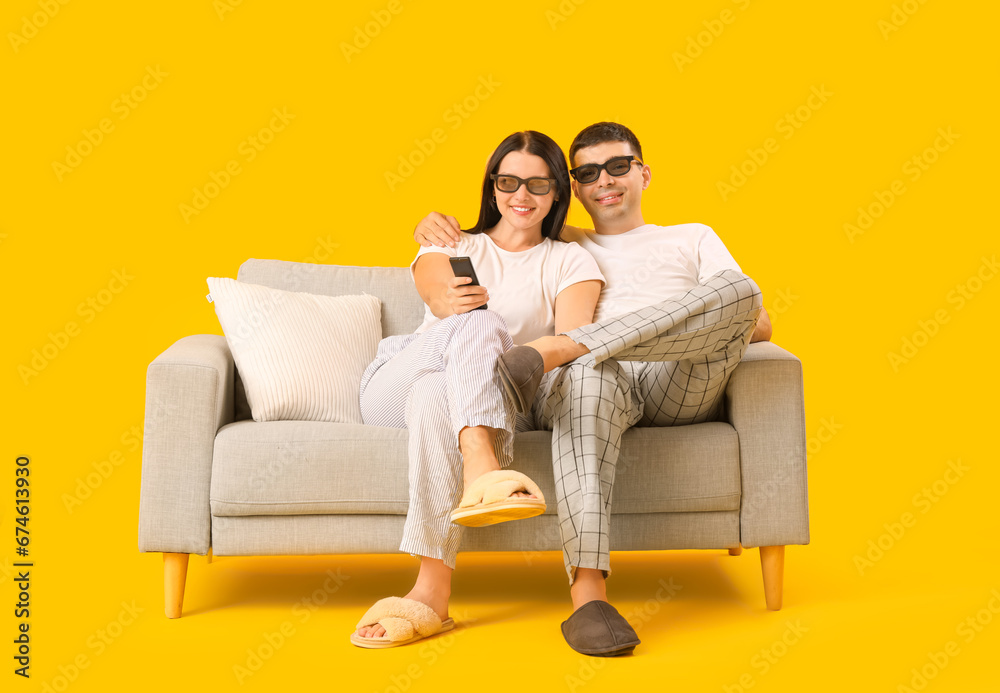 Happy young couple sitting on sofa and watching TV while sitting on sofa against yellow background