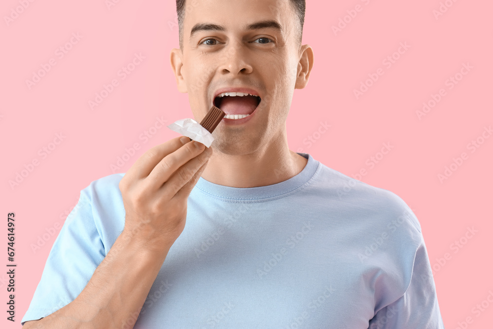 Handsome man eating chocolate on pink background, closeup