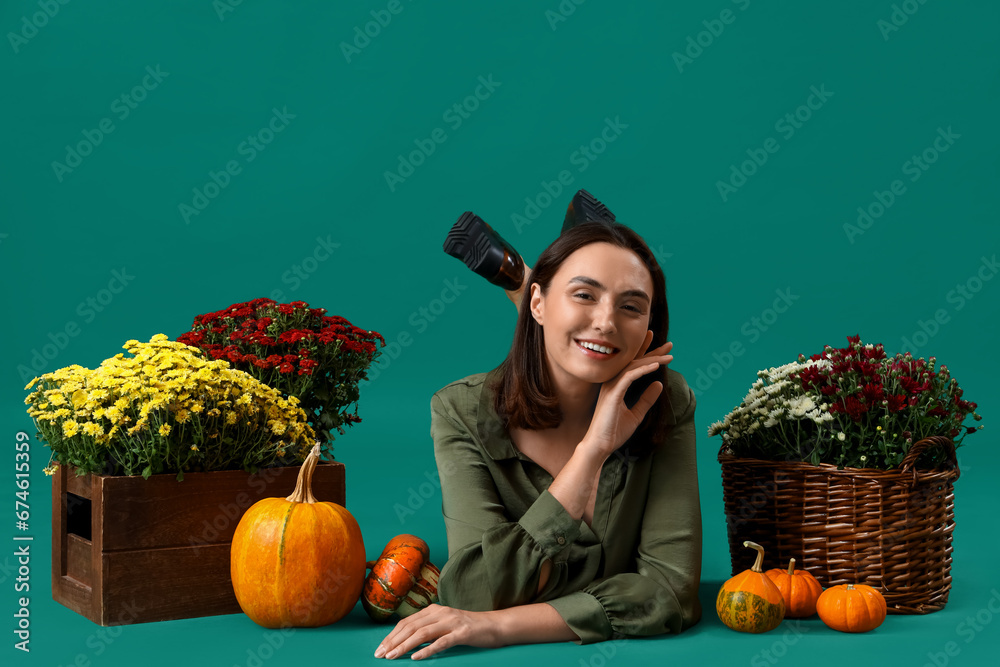 Young woman with chrysanthemum flowers and pumpkins lying on green background