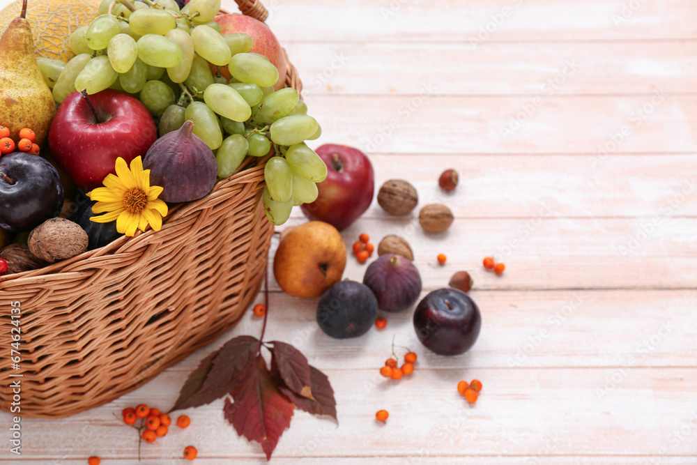 Wicker basket with different fresh fruits on white wooden background